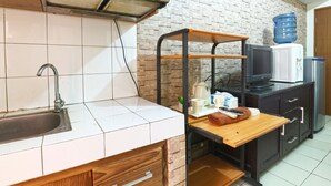 Une cuisine équipée d’un évier, d’un plan de travail en bois, d’une étagère, d’un four à micro-ondes et d’un distributeur d’eau.