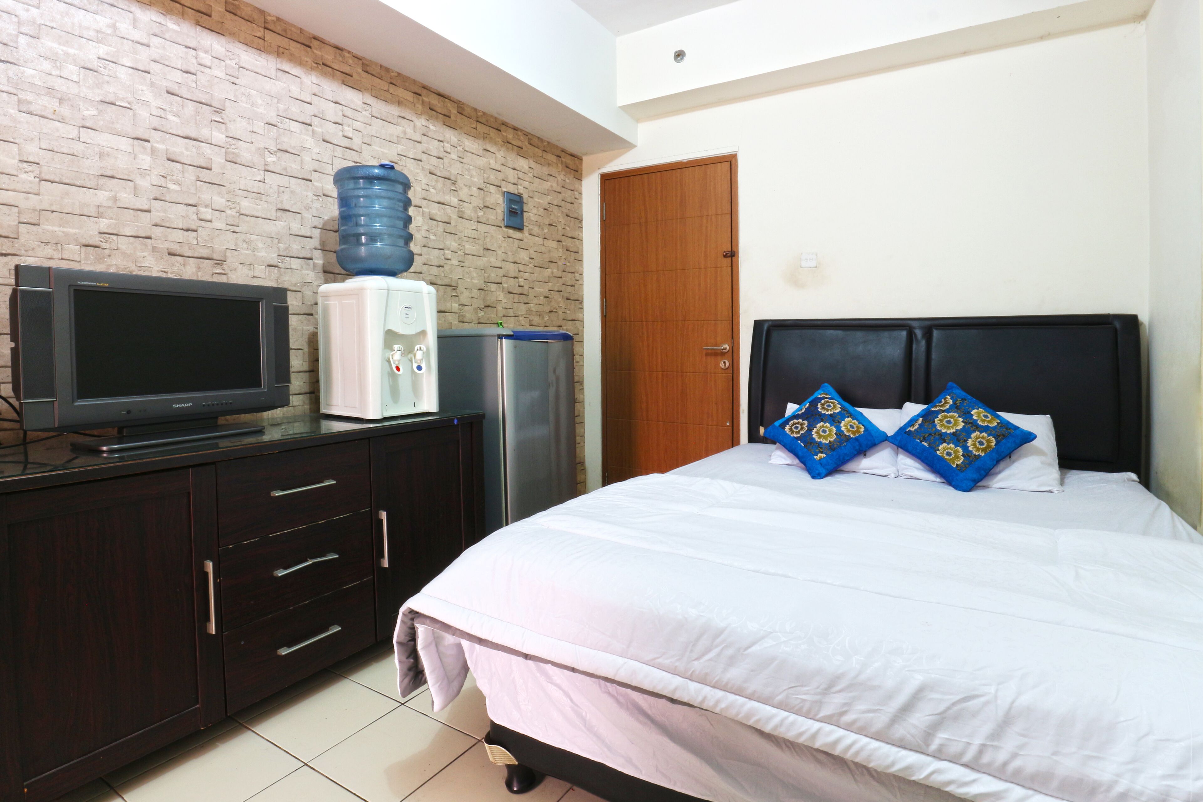 A bedroom with a bed, a television on a dresser, a water dispenser, and a wooden door.