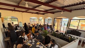 A communal dining area with tables and chairs, a water dispenser, and a view through large windows. - Hotel Posada Gutierrez (Panajachel)