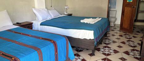 Habitación de hotel con dos camas, una mesita de noche, un ventilador en la pared, un inodoro y una puerta con un cartel.