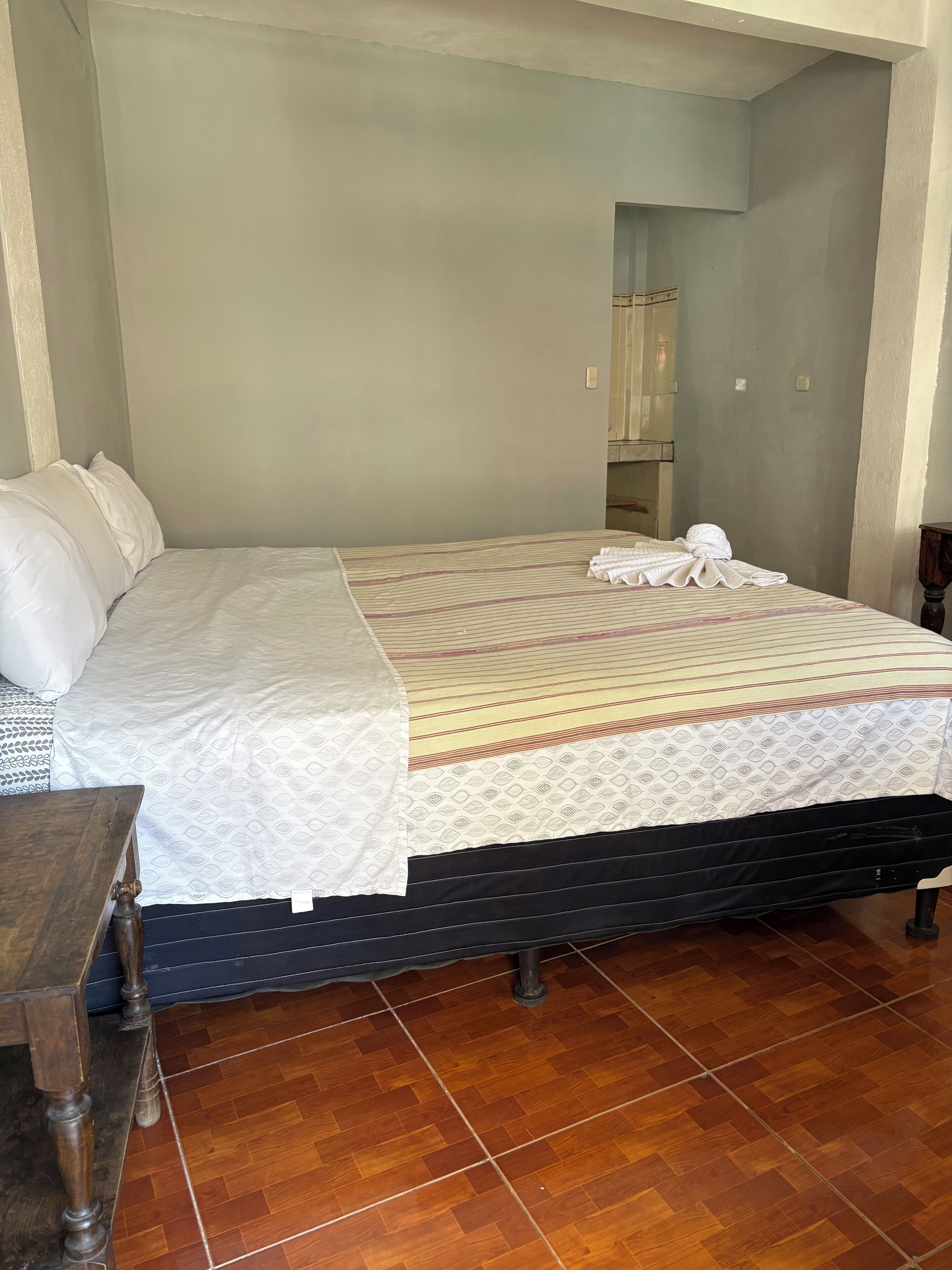 Una cama con una colcha estampada, una mesita de noche de madera y un piso de baldosas.