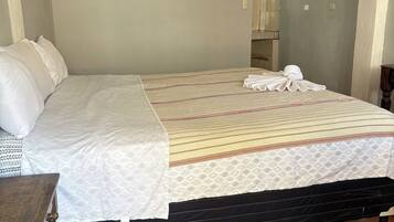 Una cama con una colcha estampada, una mesita de noche de madera y un piso de baldosas.