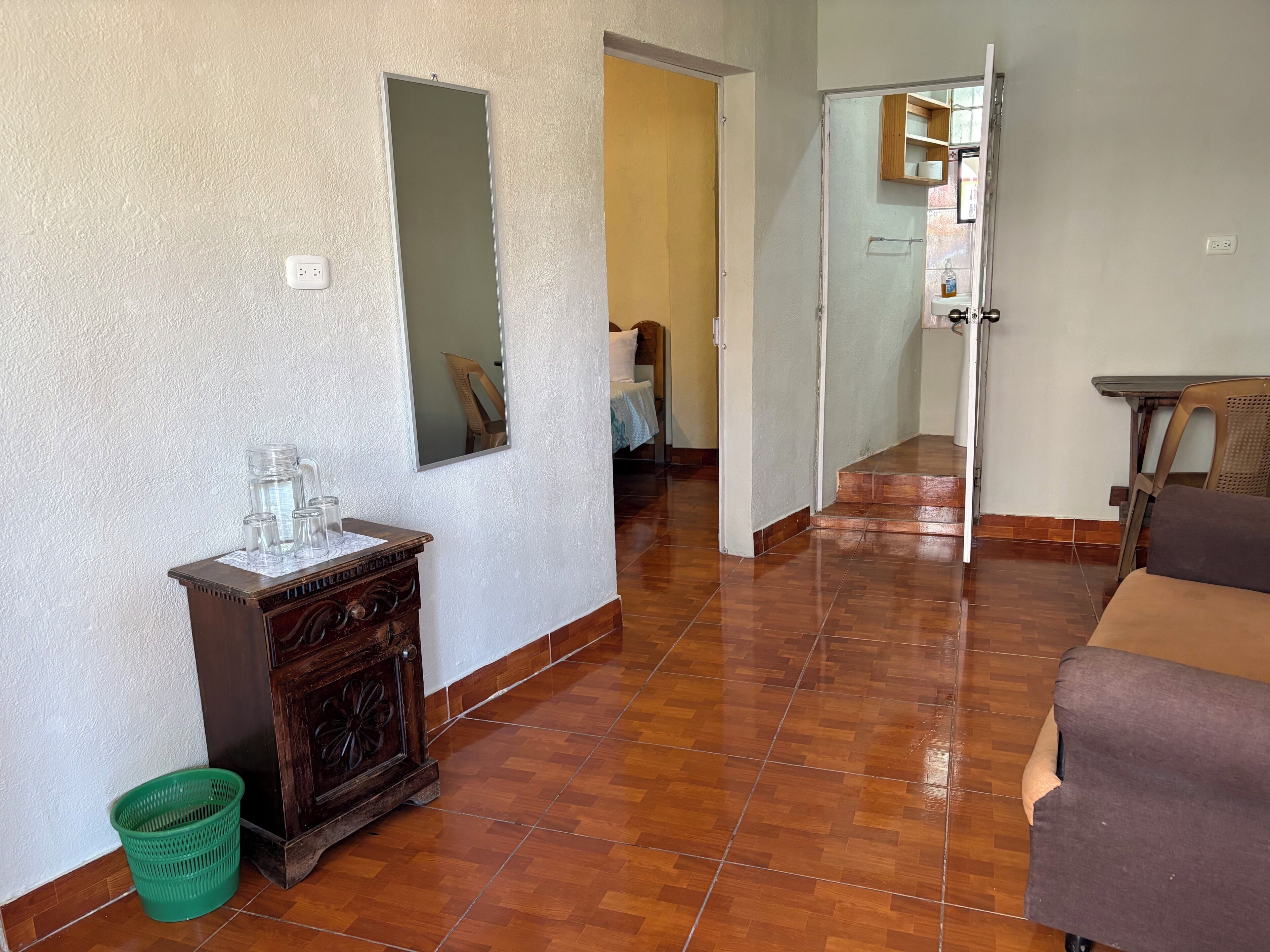 Un pasillo con suelo de madera, un espejo, un armario y una cesta verde.