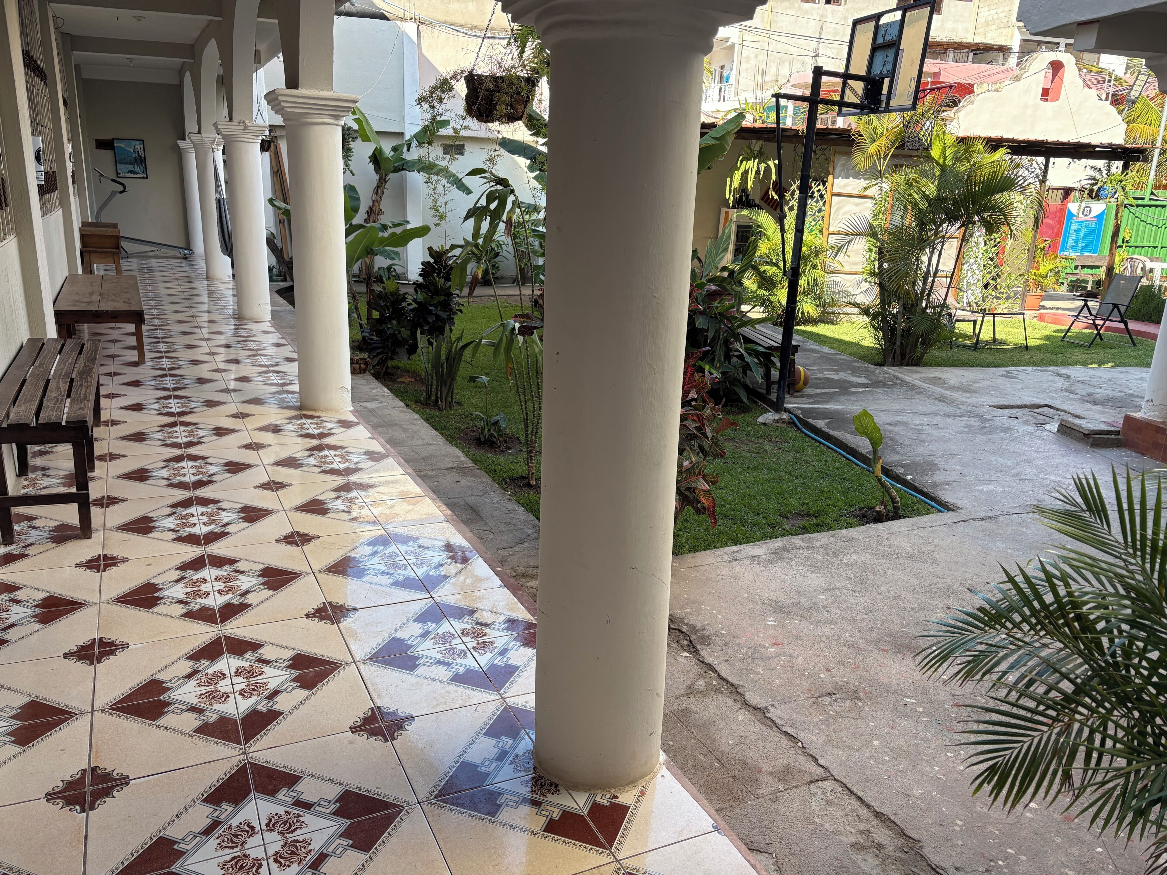 A covered outdoor area with tiled flooring, benches, and columns.