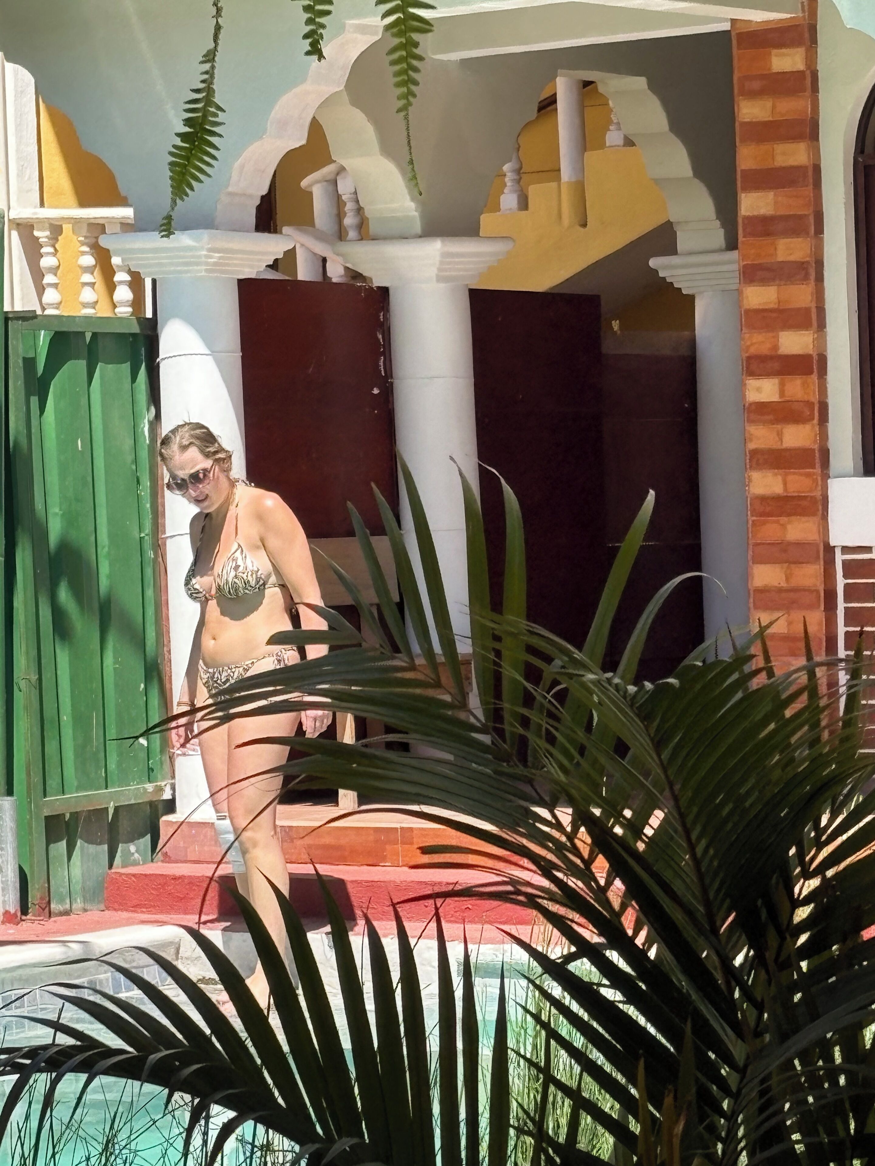 Une personne en bikini, près d’une piscine, avec un bâtiment en arrière-plan.