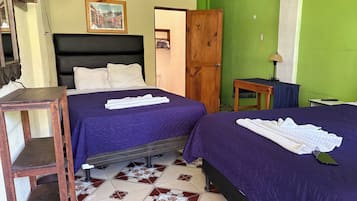 A room with two beds, a wooden nightstand, a table with a lamp, and a door leading to another room.