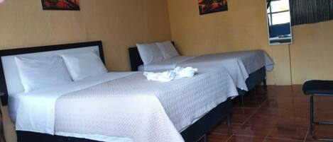 Una habitación con dos camas, una mesita pequeña y dos cuadros en la pared.