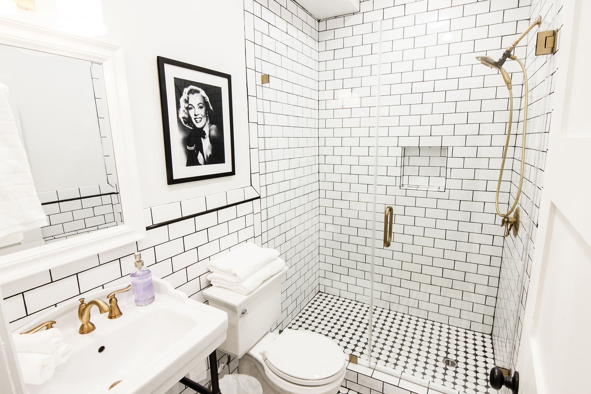 A bathroom with white subway tiles, a framed picture on the wall, a sink with gold faucets, and a shower with a gold showerhead.