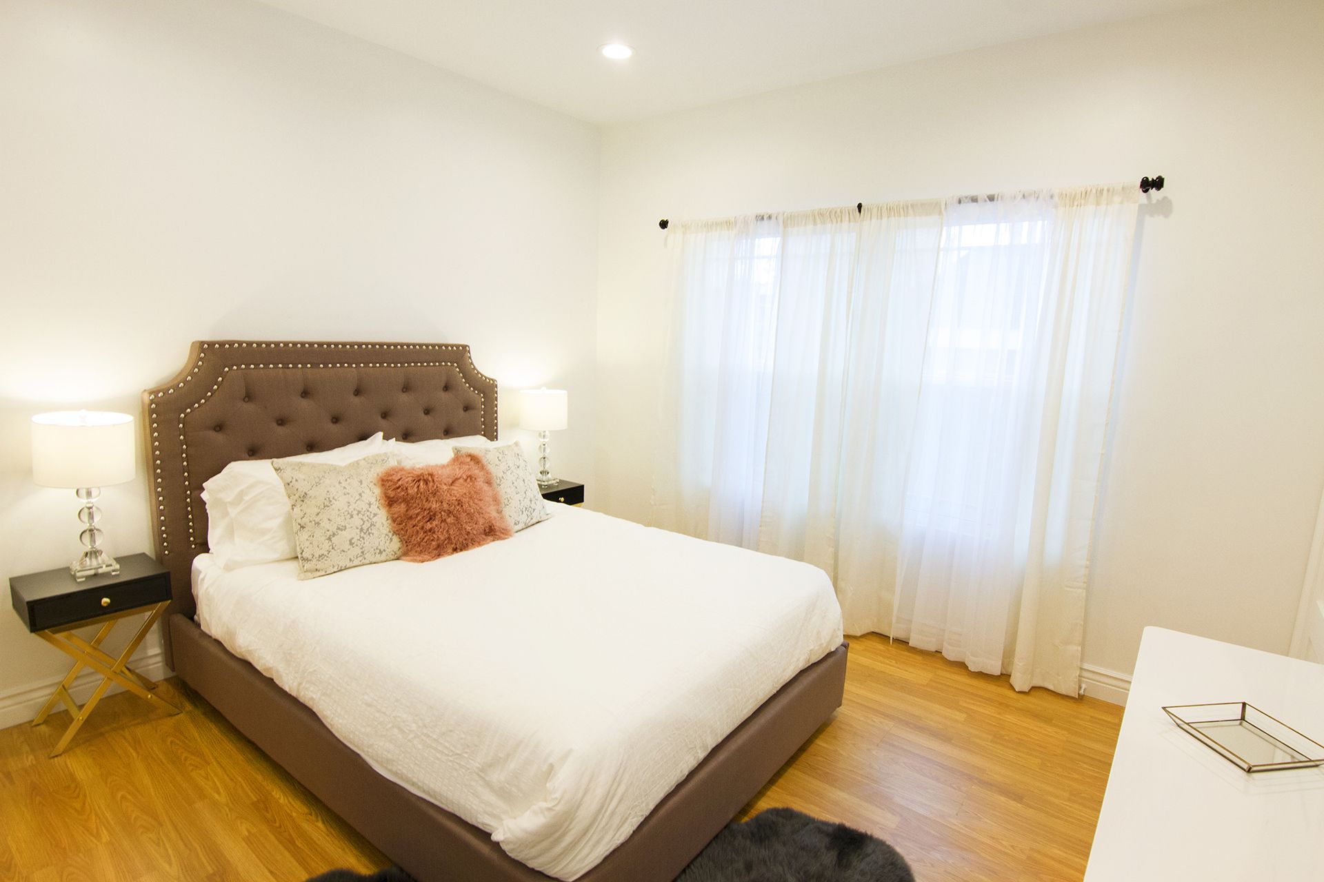 A neatly arranged bedroom with a large bed, two bedside tables, and a window with sheer curtains.