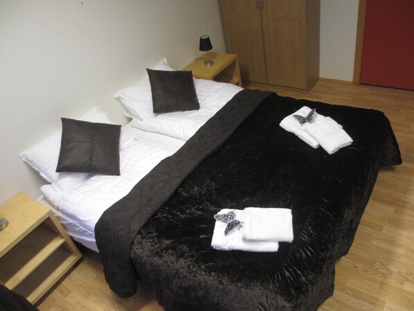 A neatly made bed with white and black bedding, a black velvet throw, and two white towels with butterfly decorations.