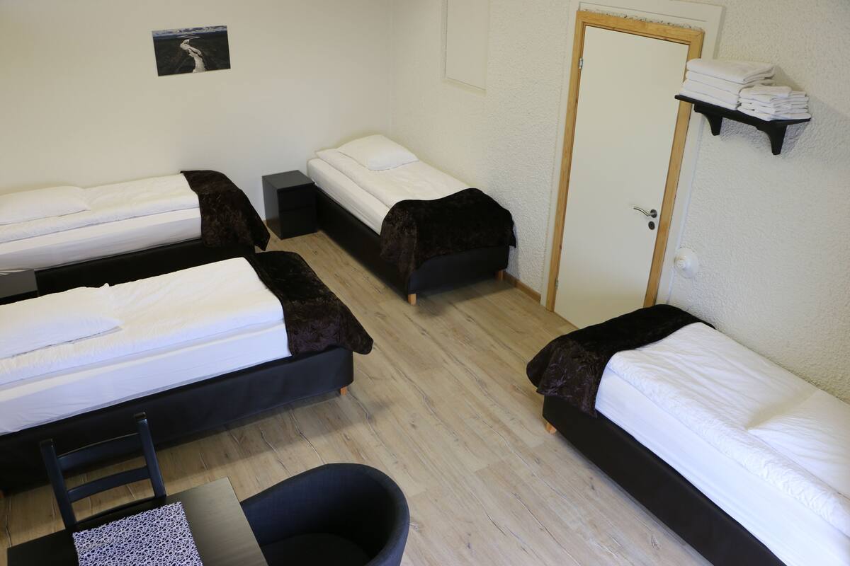 Een kamer met drie eenpersoonsbedden, een klein bureau, een stoel en een deur.