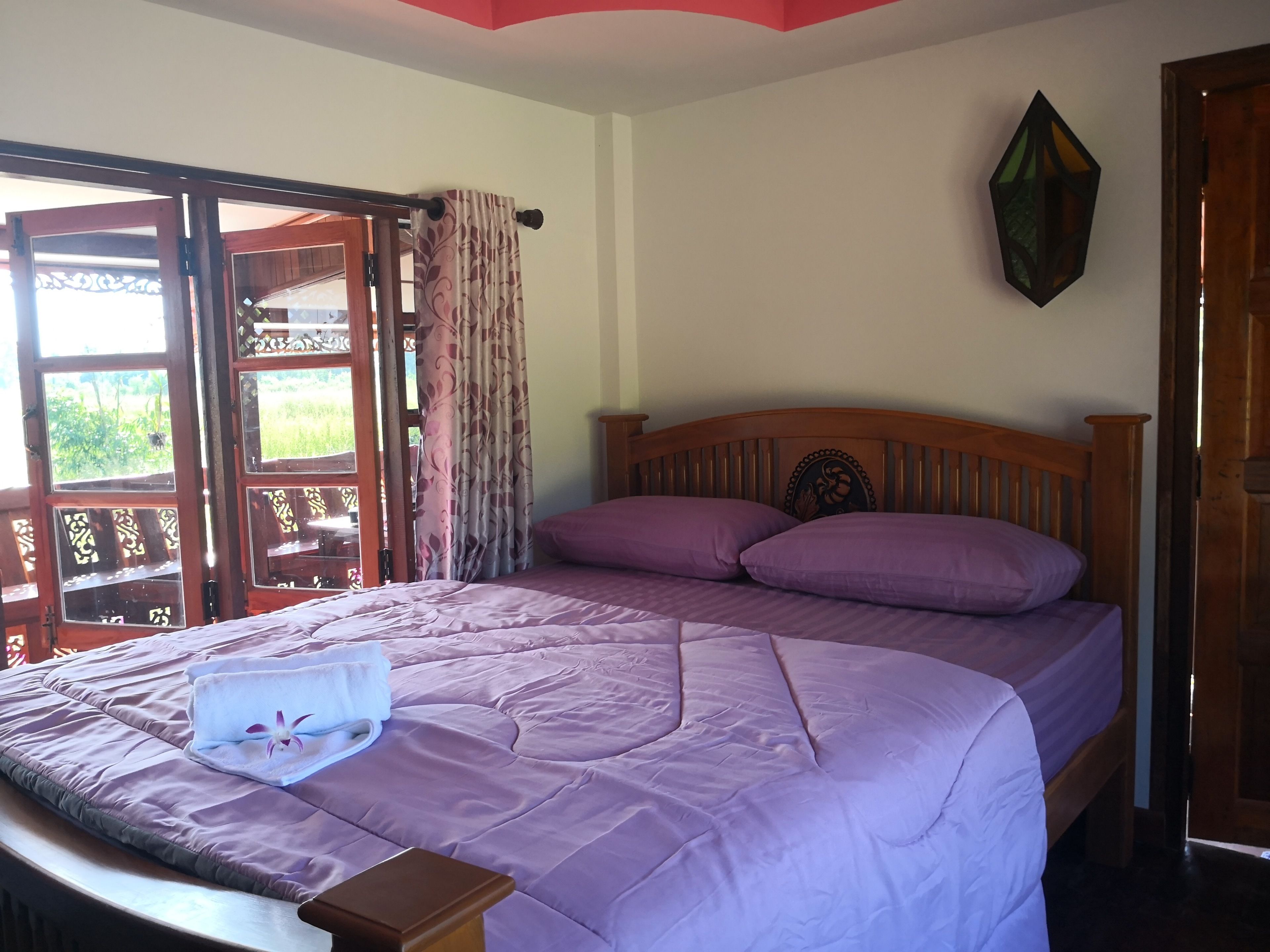 A bedroom with a bed, purple bedding, a wooden headboard, a nightstand, and a window with curtains.