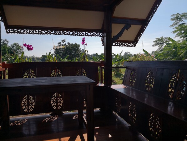 A wooden deck with intricate carvings, a bench, and hanging flowers. - Pumaka Resort (Nong Hong)
