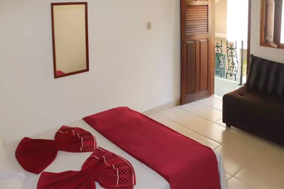 Quarto de hotel com uma cama, um cobertor vermelho e um par de chinelos vermelhos.