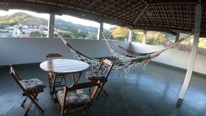 A covered patio with a hammock, a round table, and four wooden chairs. - Pousada O Meu Canto (Santa Rita de Jacutinga)