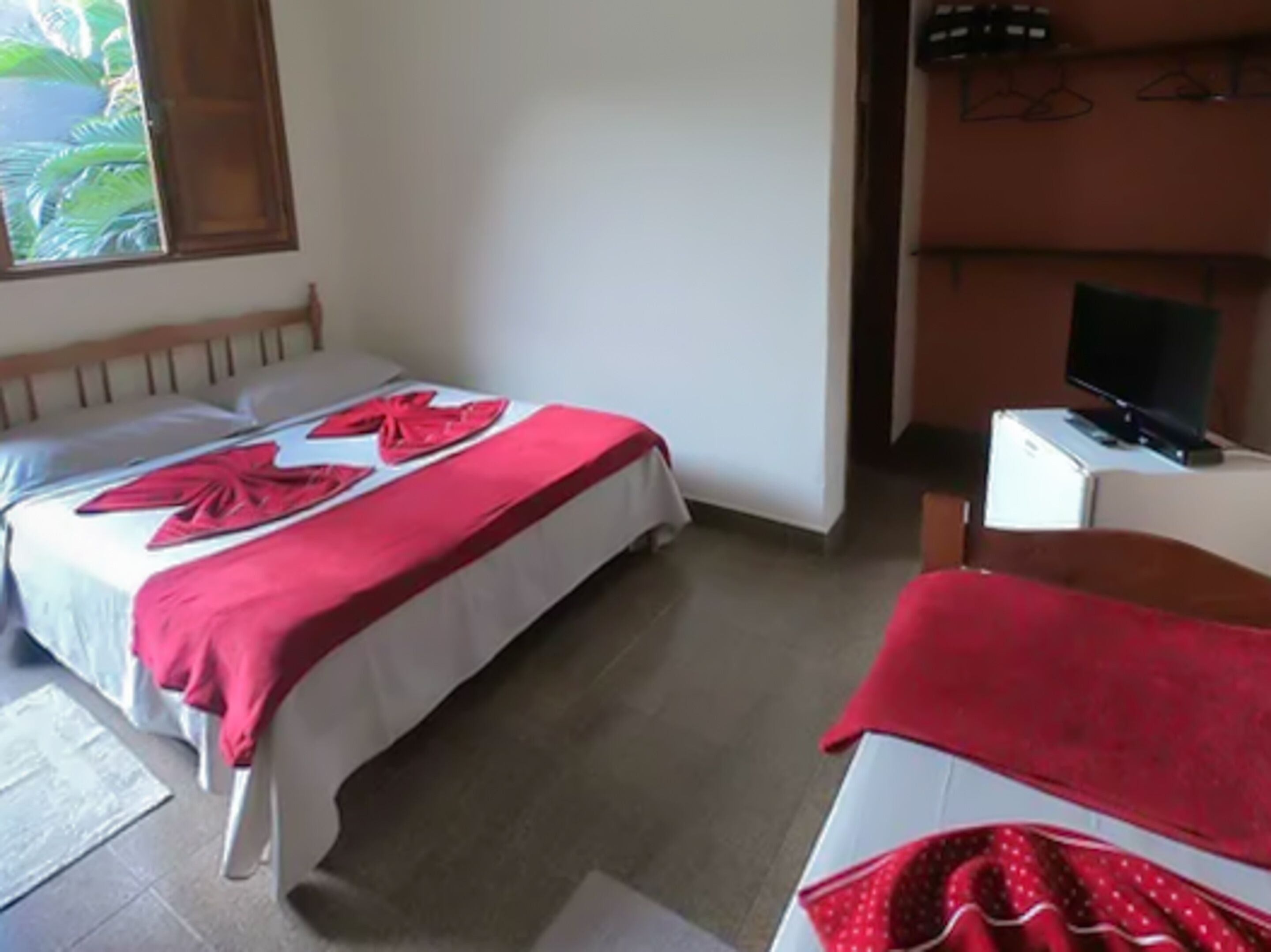 A room with two beds, a television on a table, and a window with a view of greenery.