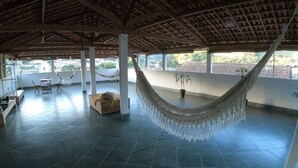 A spacious indoor area with a hammock, a table, and chairs. - Pousada O Meu Canto (Santa Rita de Jacutinga)