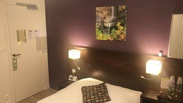 A hotel room with a bed, a nightstand with a lamp, a wall-mounted picture, and a door with a lock and key card.