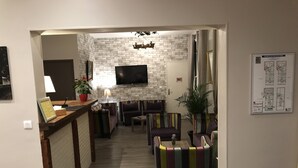 A modern living room with a brick wall, a flat-screen TV, and colorful striped sofas. - Hôtel les Iris (Les Andelys)