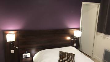 Habitación de hotel con tablero de cabecera de madera oscura, ropa de cama blanca y un cojín a cuadros, además de lámparas de noche.