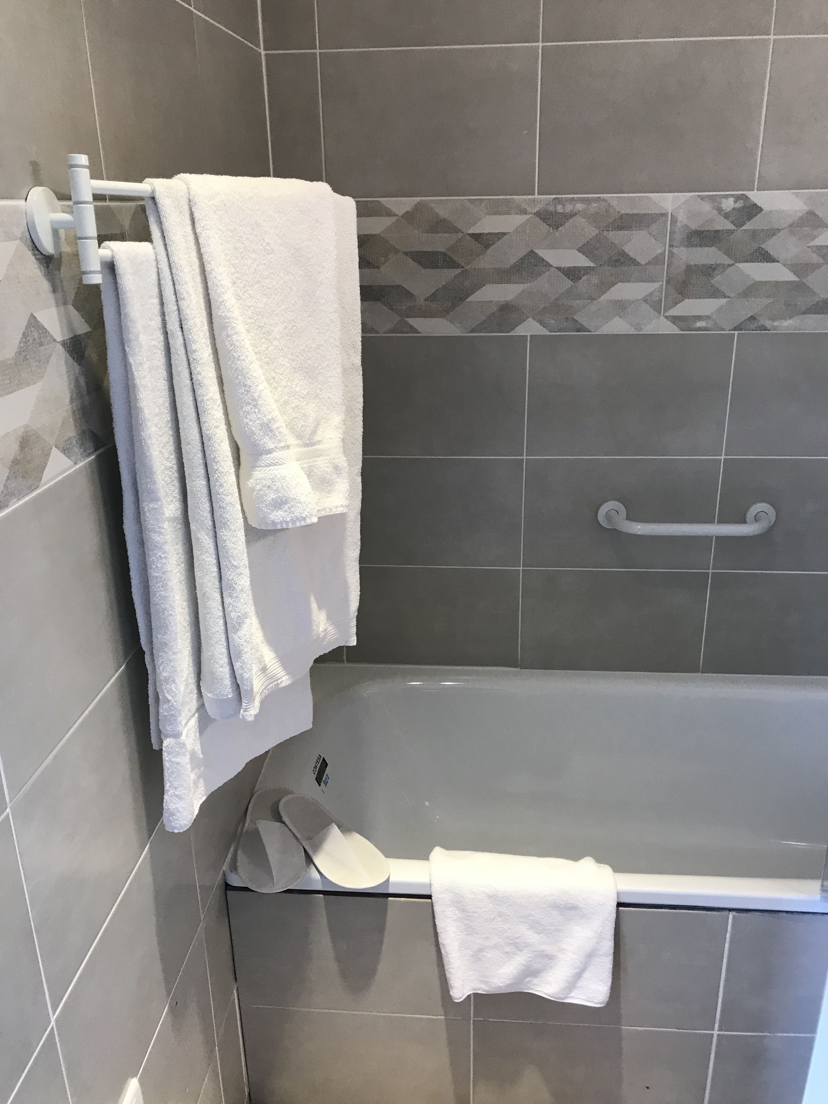 Un baño con una bañera, un perchero con varias toallas, un pasamanos y azulejos decorativos en la pared.
