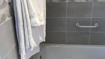 Un baño con una bañera, un perchero con varias toallas, un pasamanos y azulejos decorativos en la pared.