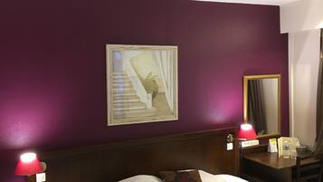 A hotel room with a bed, a nightstand with a lamp, a mirror, and a framed picture on the wall.