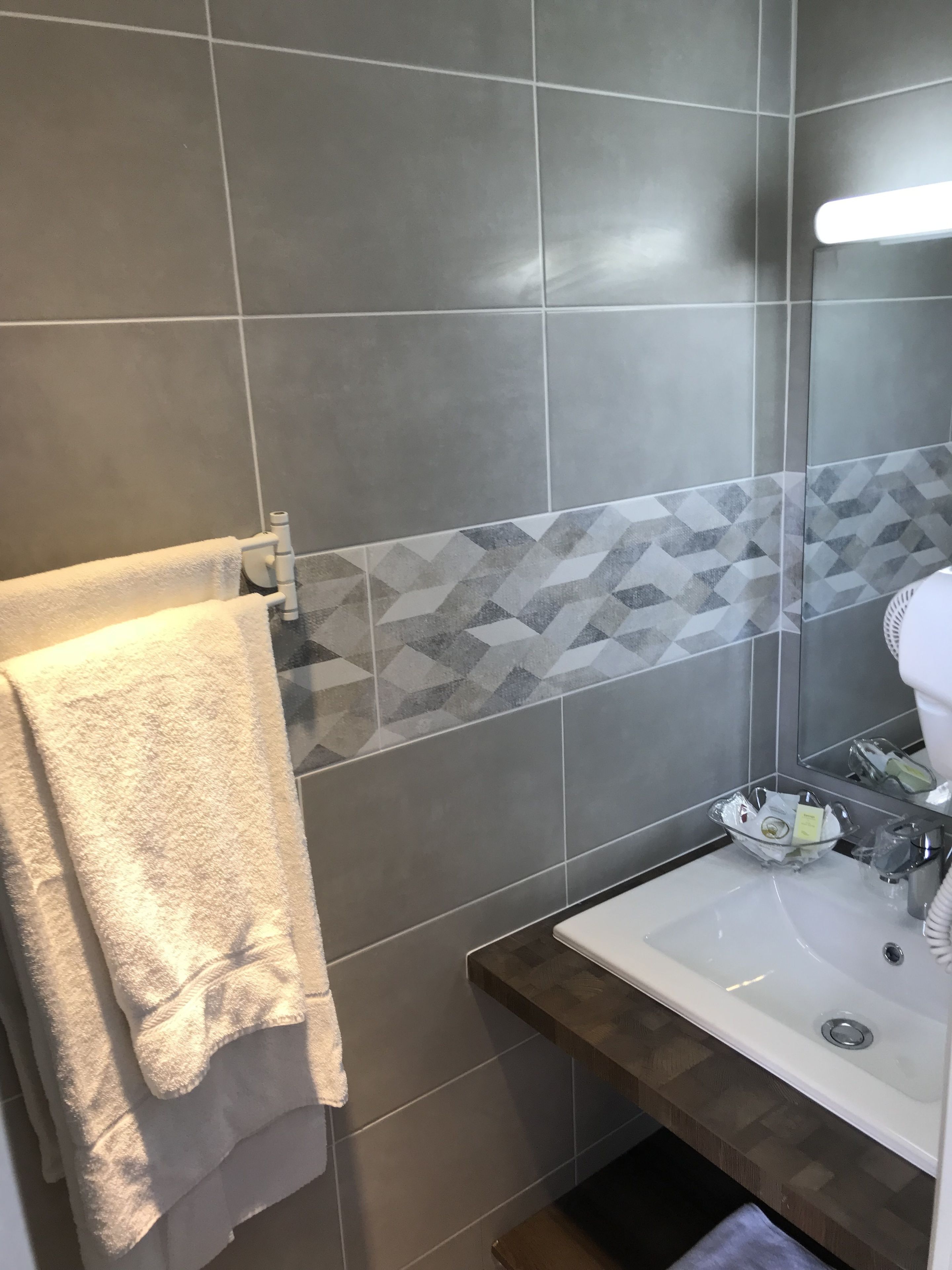 A bathroom with grey tiles, a towel rack, a sink with toiletries, and a mirror.