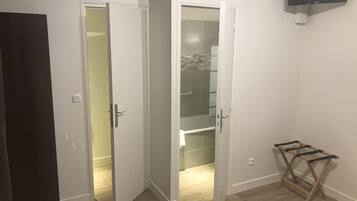 A room with a wooden floor, a white door, a closet with a glass door, and a mounted TV.