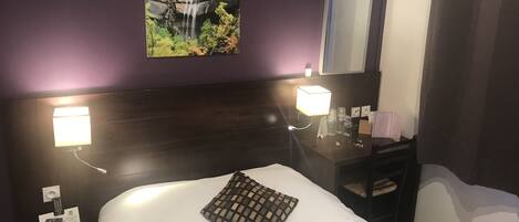 Una habitación de hotel con una cama, una mesita de noche con una lámpara, una pequeña mesa con un espejo y un cuadro de una cascada colgado en la pared.