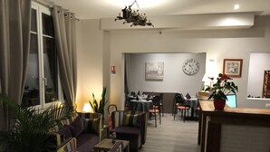 A living room with a sofa, chairs, a dining table, and a kitchen area in the background. - Hôtel les Iris (Les Andelys)