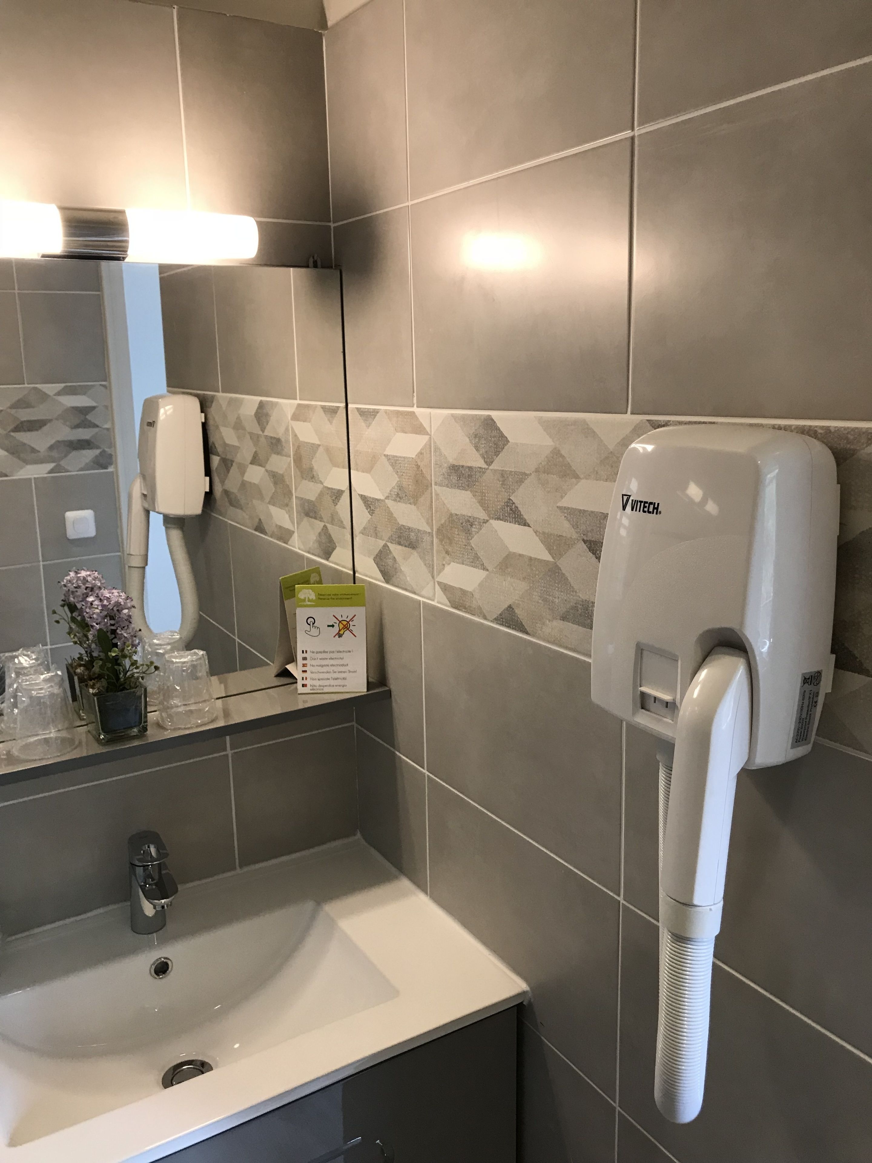 A bathroom with a sink, mirror, and a wall-mounted hair dryer.