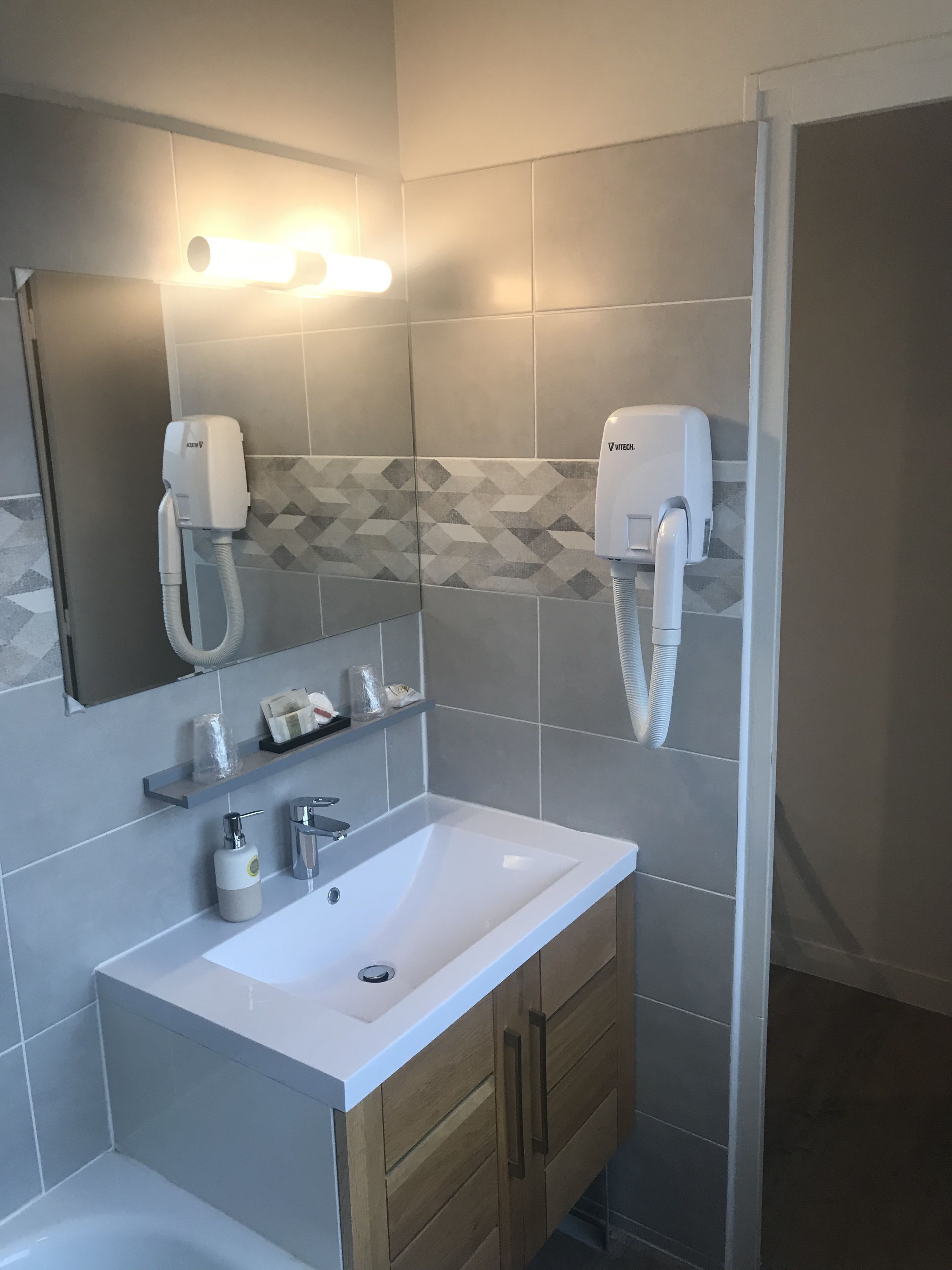 Un baño moderno con lavamanos blanco, armarios de madera y dos secadores de pelo montados en la pared.
