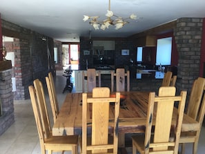 A dining area with a wooden table and chairs, a chandelier, and a kitchen in the background.