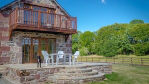 A stone building with a wooden balcony, a patio with chairs, and a dog. - Castleview - Newton Steading (Kirriemuir)