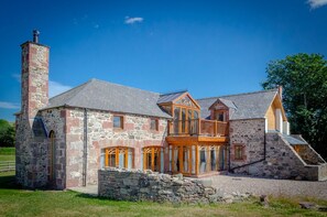 A stone house with a large balcony, a chimney, and a stone wall.