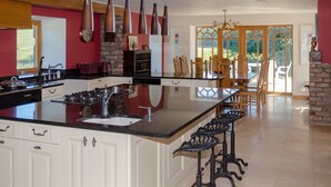 A spacious kitchen with a large island, white cabinetry, and a dining area with wooden chairs and a table. - Castleview - Newton Steading (Kirriemuir)