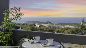 A balcony with a table and chairs, overlooking a scenic view of the sea and distant land during sunset. - Talos Luxury Suites (Chania)