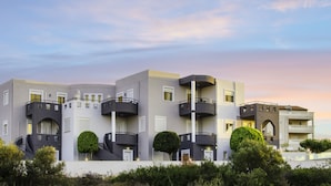 A modern multi-story building with balconies, a flat roof, and a landscaped front garden. - Talos Luxury Suites (Chania)