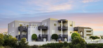 Un edificio moderno de varios pisos con balcones, techo plano y un jardín delantero ajardinado.