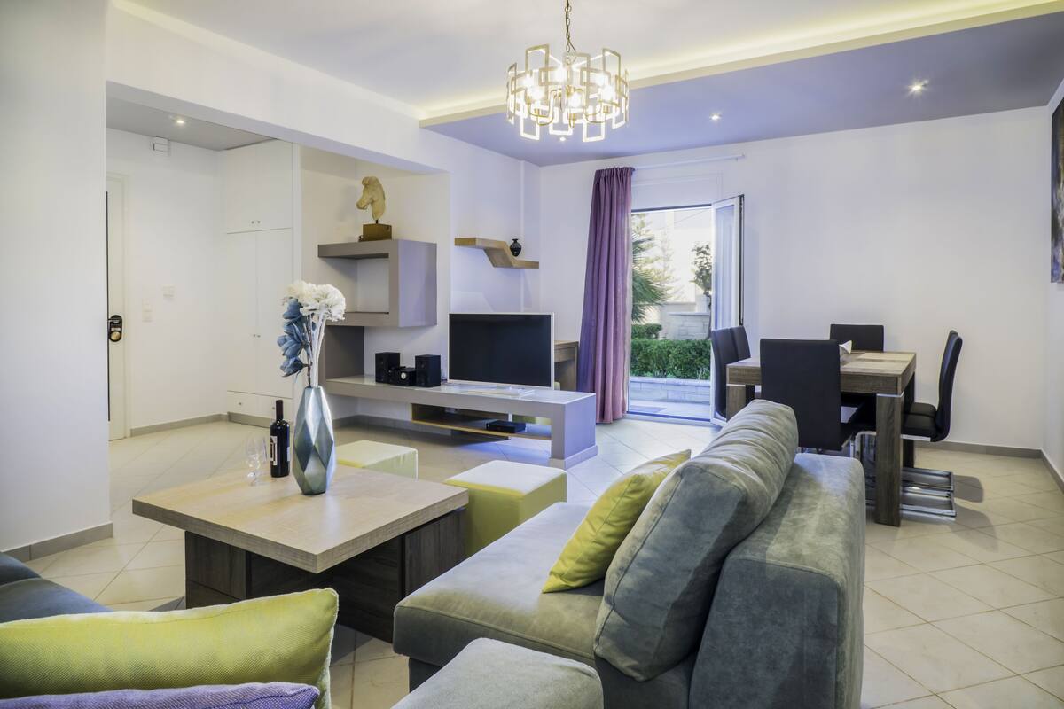 A modern living room with a sofa, coffee table, TV, and dining area.
