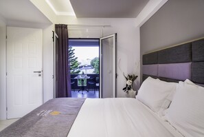 A modern hotel room with a large bed, a balcony with a table and chairs, and a view of the outside. - Talos Luxury Suites (Chania)
