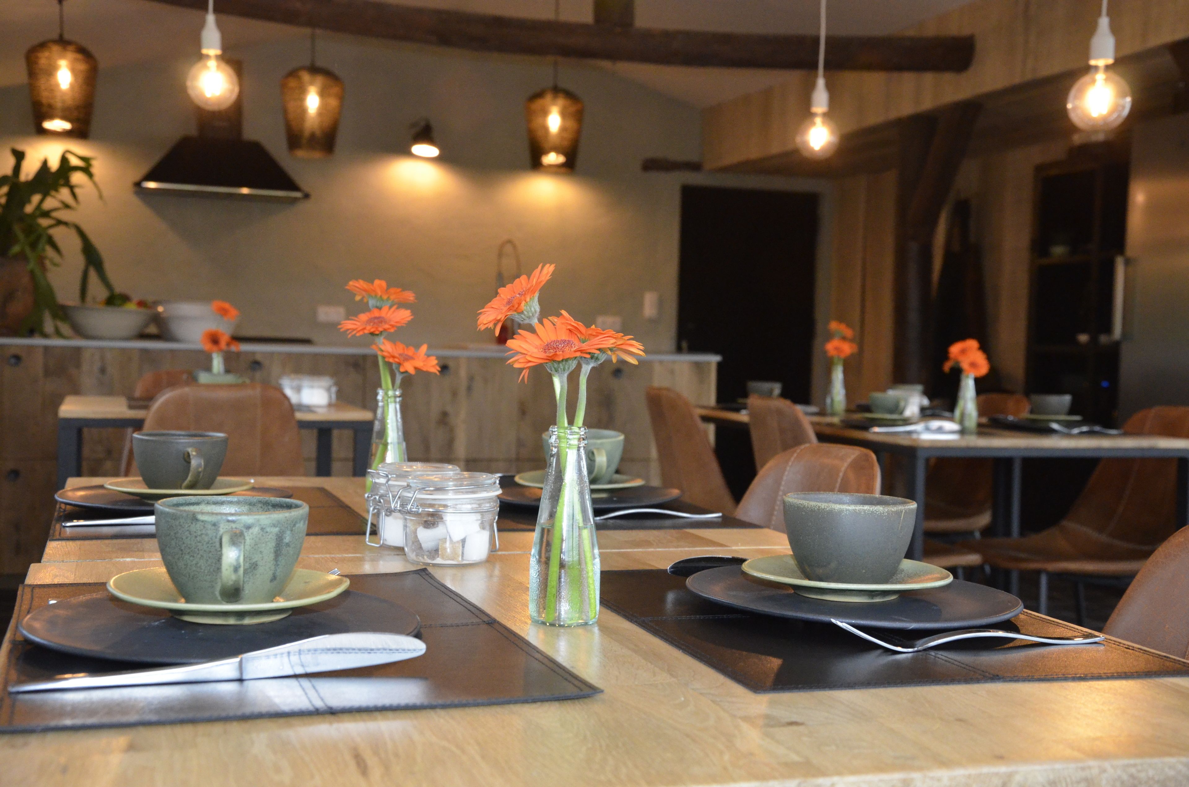 Une salle de restaurant avec des tables dressées pour le service, agrémentée de tasses, de soucoupes et de vases en céramique ornés de fleurs.