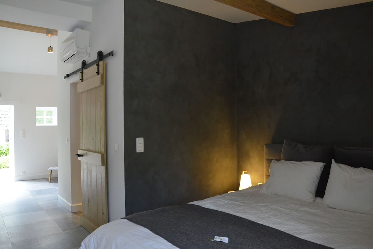 A bedroom with a bed, a wooden wardrobe, a wall-mounted air conditioner, and a small table.