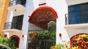 Un edificio con fachada blanca, detalles en rojo y una entrada protegida por una reja.