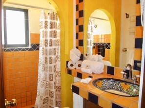 Un baño con baldosas anaranjadas y negras, una cortina de ducha estampada, un lavabo con un recipiente decorativo y un espejo que refleja la habitación.