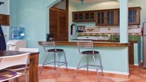 Una cocina con barra, dos taburetes de bar, dispensador de agua y cafetera.