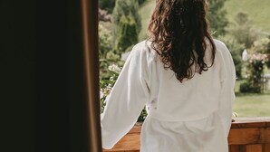 A person in a white robe standing on a wooden deck, overlooking a lush green landscape with trees and hills. - Hotel Rosenhof Murau (Murau)