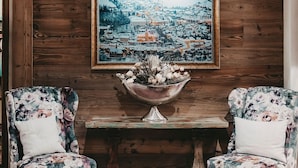 A wooden wall with a framed landscape painting, two floral armchairs, and a metal bowl with flowers on a wooden table. - Hotel Rosenhof Murau (Murau)