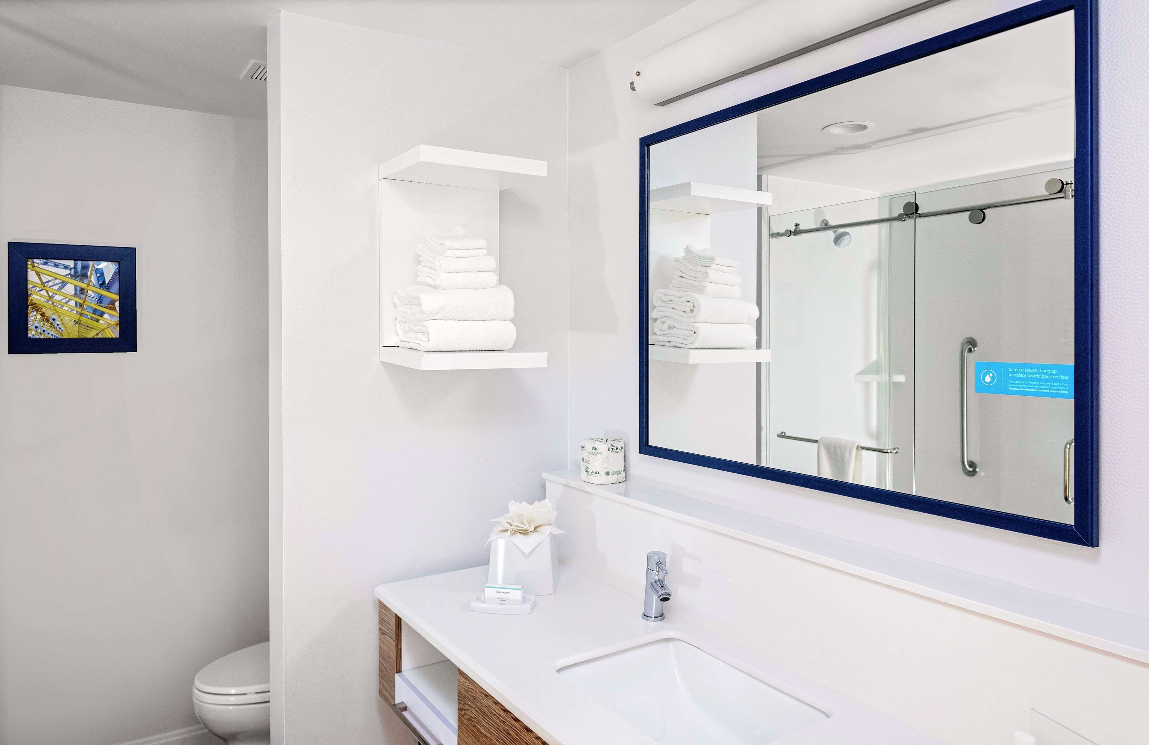 A modern bathroom with a large mirror, white shelves with towels, a toilet, and a sink.